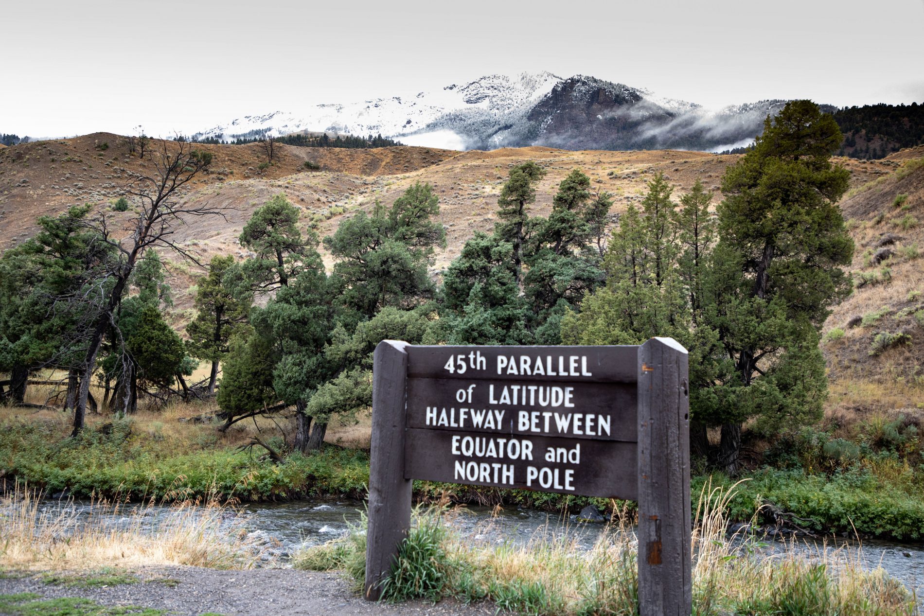 45th Parallel marker near the Northern Entrance to Yellowstone with snowcapped mountains in the background.