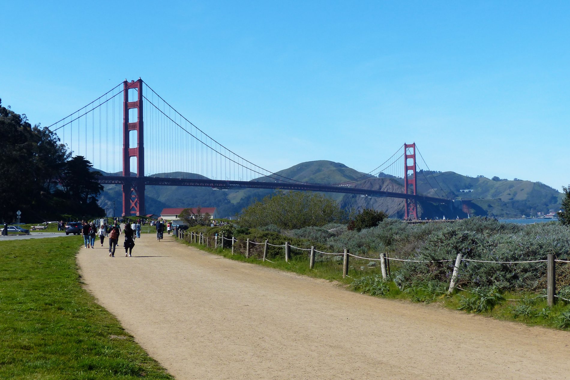 People walking along the Golden Gate Promenade through Crissy Field with the Golden Gate Bridge in the background.
