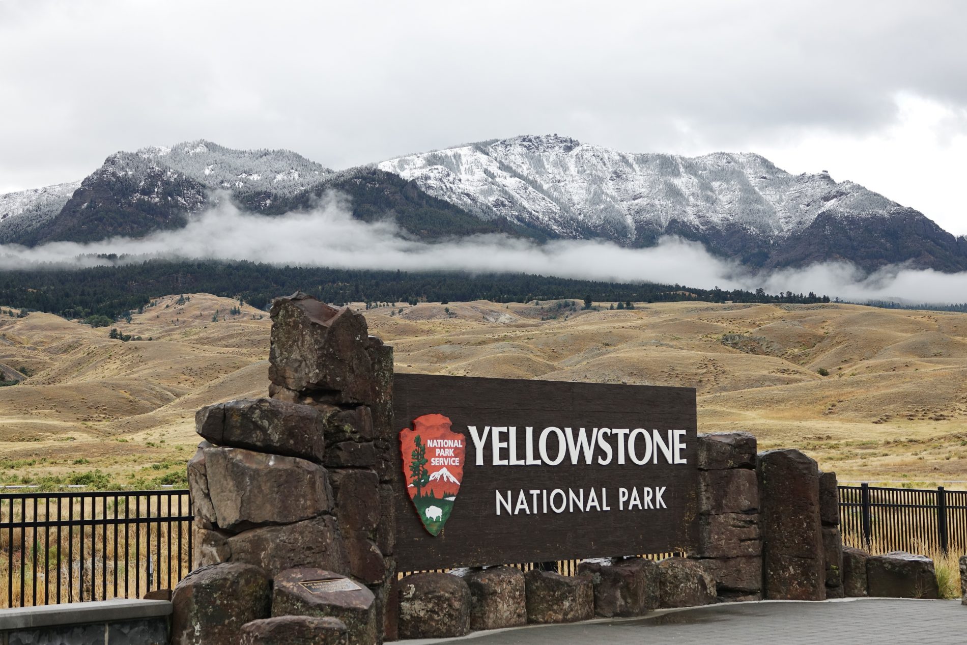 Sign at the Northern Entrance to Yellowstone National Park with snow-capped mountains in the background.