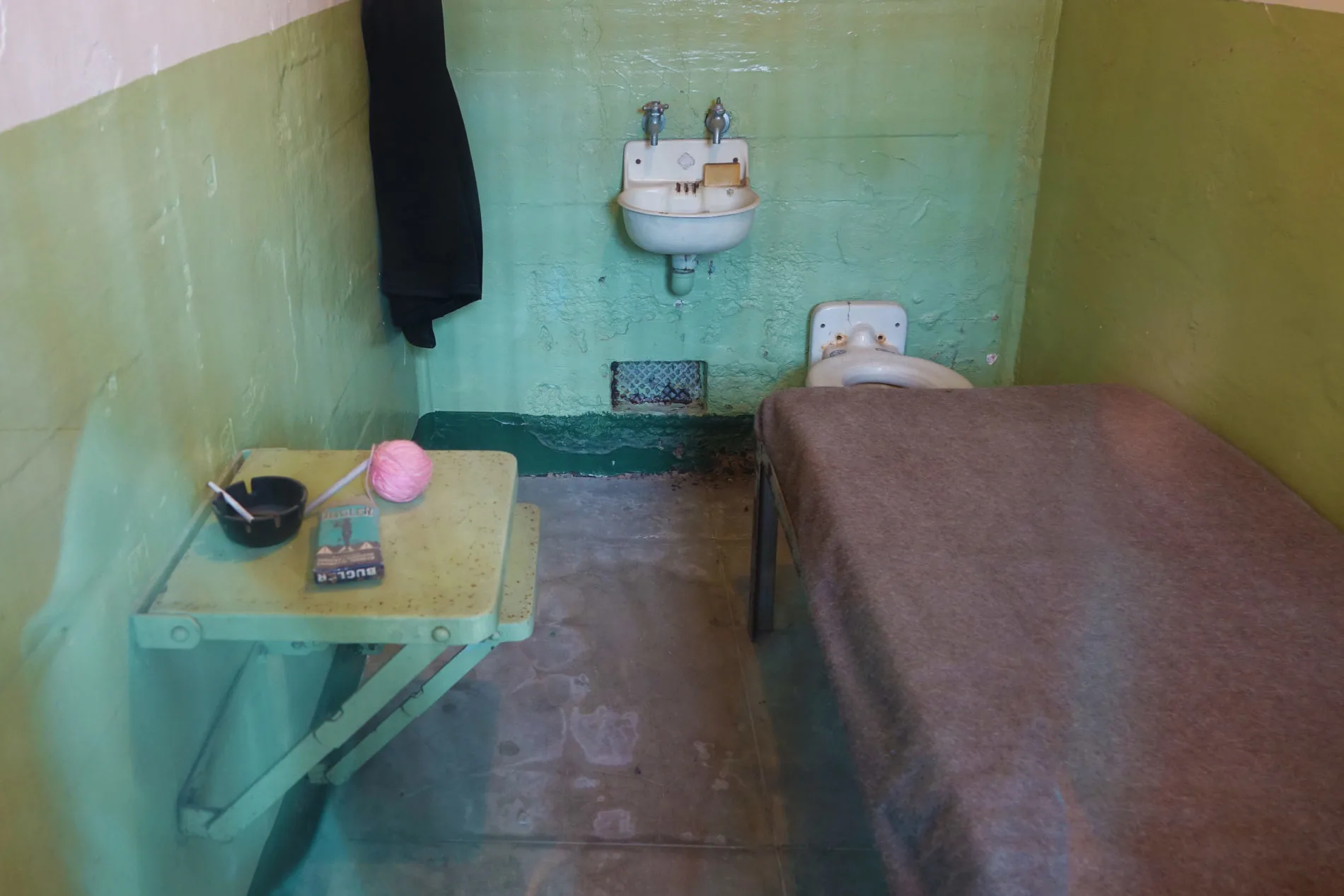 An Alcatraz prison cell with an ashtray, cigarettes, and ball of yarn on the table. Some inmates passed the time knitting.