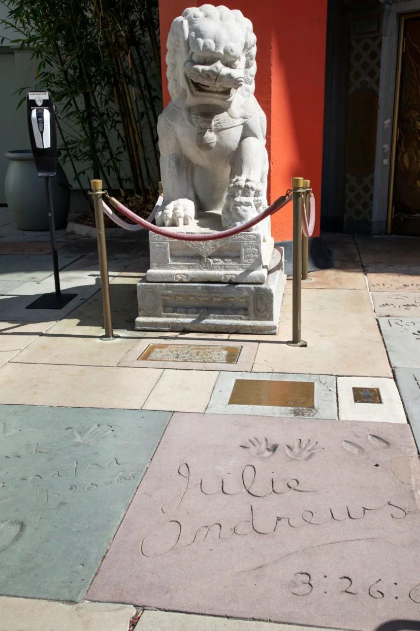 A guardian lion looks down smiling at Julie Andrews handprint in the forecourt of the stars in Hollywood, CA.